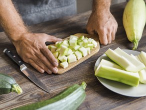 Zucchini harvest. Man slices zucchini cubes for freezing on wooden table. Farm organic zucchini