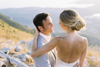 Bride sits on the lap of groom, hugging his shoulders.