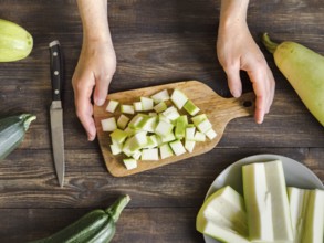 Zucchini harvest. Woman slices zucchini cubes for freezing on wooden table. Farm organic zucchini