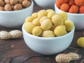 Peanut snack for beer, wine, party bar. Salted peanuts in yellow cheese glaze on brown wooden table