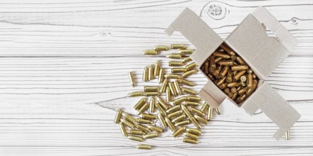 Top down view, carton box with yellow brass ammunition bullets on white wooden desk, banner - space