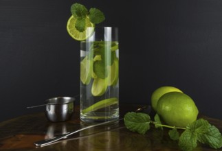 Glass of Mojito cocktail with mint and lime on a black board with fresh limes. Sparkling refreshing