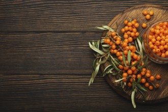 Sea buckthorn ripe berries in glass jar and branches with leaves top view on dark wooden rustic