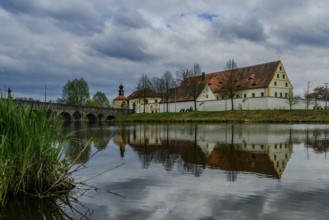 Old building and bridge reflected in a river under a cloudy sky, Tirschenreuth, Upper Palatinate,