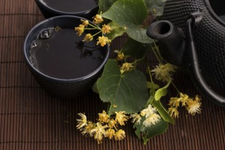 Teapot and cup with linden tea and flowers