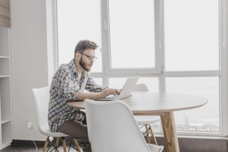 Man in a checkered shirt working on a laptop in a bright, modern room