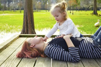 Daughter and mother playing together in the park lake pier
