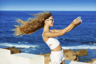 Blond kid teen girl photo selfie on smartphone in a beach at Mediterranean