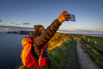 Female hiker taking a selfie, Cliffs of Moher, The Burren, County Clare, Ireland, United Kingdom,