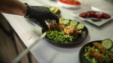 Gloved chef preparing a plate of chicken tikka garnished with fresh cucumber and lettuce in an