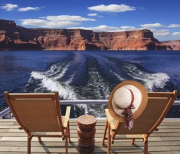 Waves from the boat cut through the Lake Powell. At the stern of the vessel are two deck chairs. On