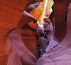 A thin ray of sunlight illuminates the sandy bottom of the canyon. Noon in a red-orange Antelope