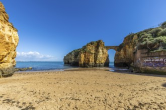 Yellow rocks and cliffs on a sandy beach. A bay by the sea, over which the old stone bridge of the