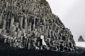 A wedding couple stands on a wall of stone pillars. The bride and groom are hugging on basalt
