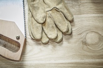 Safety gloves handsaw on wooden board top view construction concept