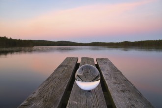 Glass ball on a wooden pier at a Swedish lake at evening hour. Nature shot from Scandinavia