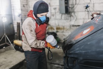 Worker spray painting a car hood in a workshop environment