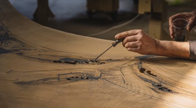 Hands adding resin to wood, focusing on intricate detailing and texture in a workshop setting