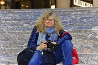 Woman sitting casually with camera on stairs and seems to concentrate on photography, Manhattan,