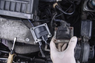 Close-up of a hand holding a car ignition coil in an engine