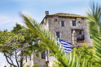 Ancient Ouranoupolis Tower on Athos peninsula in Halkidiki, flag of Greece. View through the palm