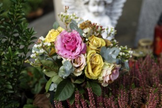 Withered pastel-coloured roses lie on a grave, a white angel in the blurred background