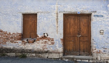 Exterior of an old village house with blue stoned wall and closed vitnage door and window