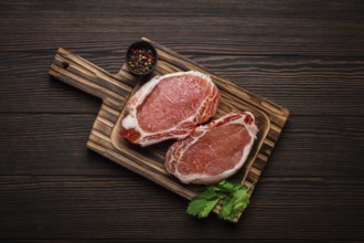 Cut raw meat pork steaks with seasonings on kitchen cutting board, rustic wooden background top
