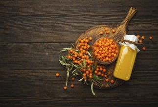 Sea buckthorn healthy drink in bottle, ripe berries in glass jar and branches with leaves top view