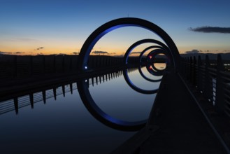 A view of the Falkirk Wheel at sunset with lights in different bright colors