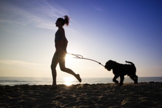 Girl running in the company of her dog on the seashore shot against the light