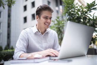 Happy handsome businessman looking at computer screen while typing something on laptop keyboard