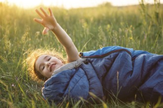 A child sleeps in a sleeping bag on the grass in a camping trip, eco-friendly outdoor recreation,