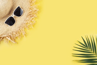 Vacation travel planning simple theme of straw hat sunglasses and palm leaves on uniform yellow