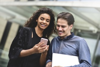 Business man and woman looking at smartphone together on building background in city outdoor