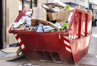 Red metallic container filled with cardboard trash in front of a shop downtown