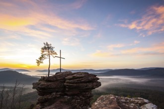 Landscape shot of nature in the morning. Mist in the valley and a summit cross on a sandstone cliff
