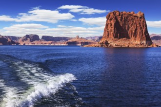 Foamy trace of a motor boat crosses the emerald waters. In the distance the coast of red sandstone.