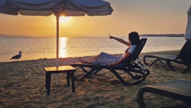 Young woman sitting on a sunbed at the beach pointing forefinger to the sunrise over the horizon.