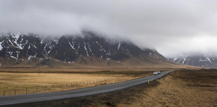 Straight highway country road with cars moving and mountains covered in mist in Iceland. Road is