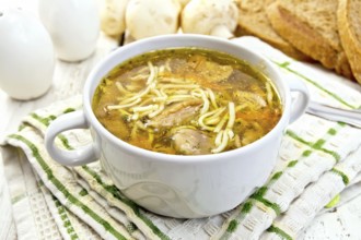 Soup with noodles and mushrooms in a white bowl on a napkin, bread on a wooden boards background