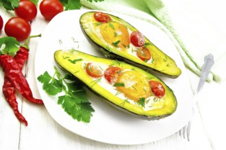 Scrambled eggs with cherry tomatoes in two halves of avocado in a plate, towel and fork on white