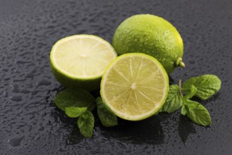 Green limes with mint and water drops on black background