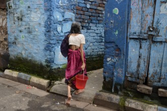 Woman with bucket walking in narrow lane, Kolkata, West Bengal, India, Asia