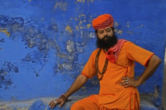Priest saffron sitting against blue wall, Jodhpur, Rajasthan, India, Asia
