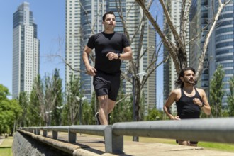 Two latin men running in a park surrounded by modern skyscrapers