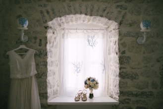 The bride's wedding dress by the window with the bride's bouquet and sandals on the windowsill.