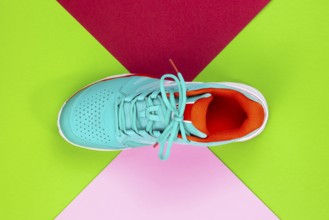 Red, cyan, white new tennis shoe in studio shot over green, pink, purple background. Directly from