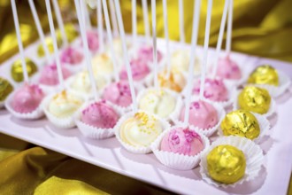 Different colourful candies on a stick. Bonbons wrapped in golden foil. Yellow, pink, white.