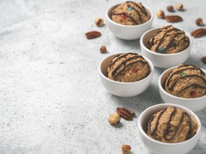 Safe-to-eat raw monster cookie dough in small portion bowl and nuts on gray cement background.
